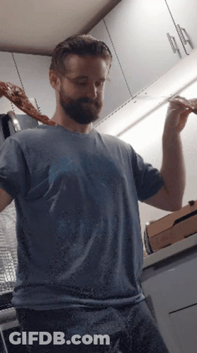 A Man In A Blue Shirt Is Holding A Slice Of Pizza In His Hand GIF