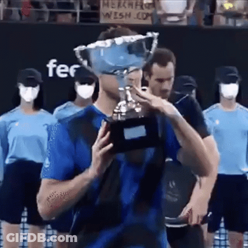 A Man In A Blue Shirt Is Holding A Trophy In Front Of A Crowd . GIF