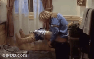 A Man In A Blue Shirt Is Holding A Woman 'S Leg In A Room . GIF