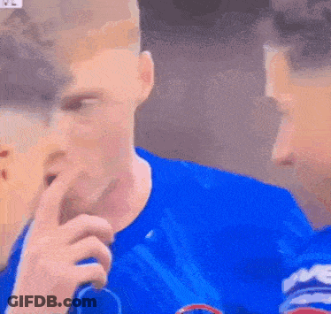 A Man In A Blue Shirt Is Holding His Finger To His Mouth . GIF