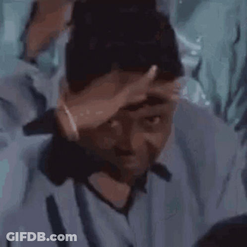 A Man In A Blue Shirt Is Holding His Hand To His Head . GIF