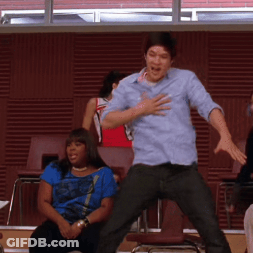 A Man In A Blue Shirt Is Jumping In The Air While A Woman Sits Behind Him GIF