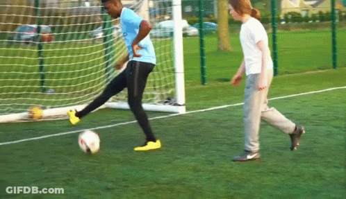 A Man In A Blue Shirt Is Kicking A Soccer Ball In Front Of A Goal GIF