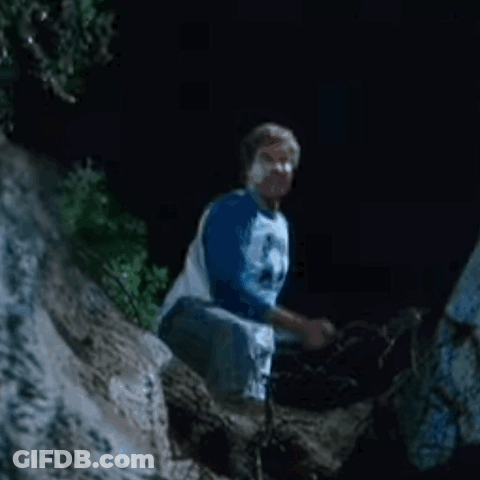 A Man In A Blue Shirt Is Kneeling Down On A Rock At Night . GIF