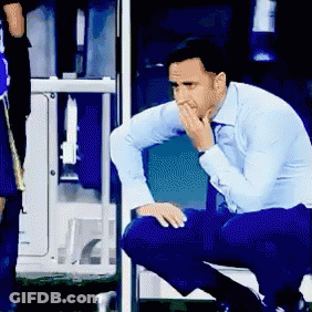 A Man In A Blue Shirt Is Kneeling Down With His Hand On His Face GIF