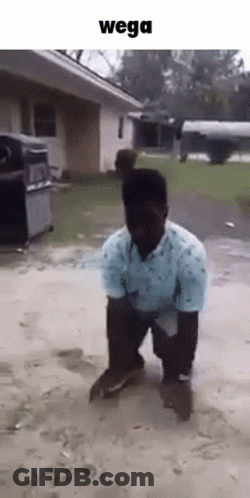 A Man In A Blue Shirt Is Kneeling On The Ground In Front Of A House With The Words Wega Above Him . GIF