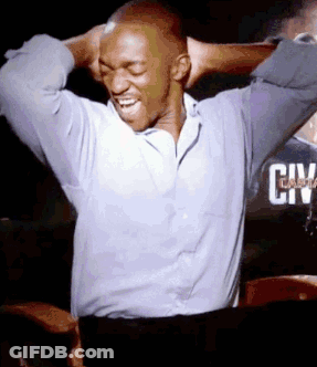 A Man In A Blue Shirt Is Laughing With His Hands Behind His Head In Front Of A Sign That Says City GIF