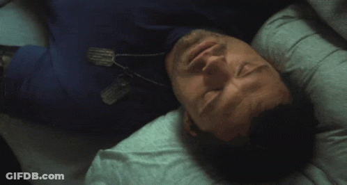 A Man In A Blue Shirt Is Laying On His Back With A Dog Tag Around His Neck GIF