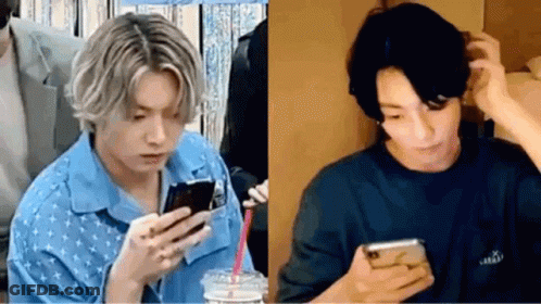 A Man In A Blue Shirt Is Looking At A Cell Phone Next To A Man In A Black Shirt . GIF