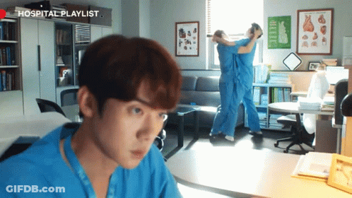 A Man In A Blue Shirt Is Looking At Another Man In A Hospital Playlist Room GIF