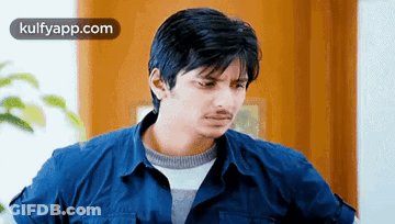A Man In A Blue Shirt Is Looking At The Camera . GIF