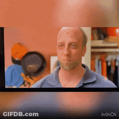 A Man In A Blue Shirt Is Looking At The Camera With A Pan Behind Him GIF