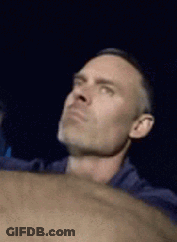A Man In A Blue Shirt Is Looking Up At Something In The Dark . GIF
