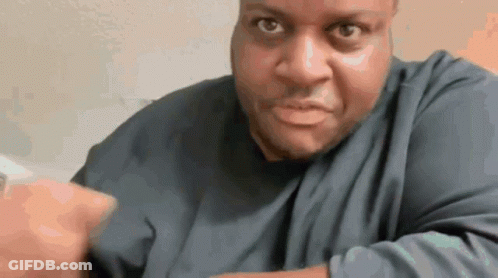 A Man In A Blue Shirt Is Making A Funny Face And Pointing At The Camera . GIF