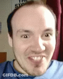 A Man In A Blue Shirt Is Making A Funny Face In Front Of A Sign That Says The Stooges GIF