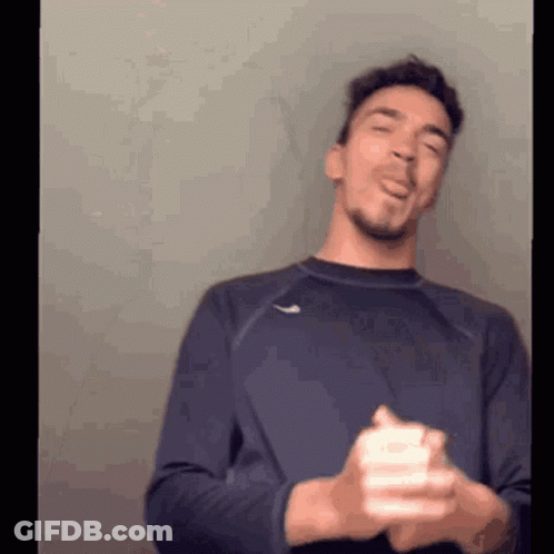 A Man In A Blue Shirt Is Making A Funny Face While Holding A White Object In His Hands . GIF