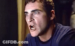 A Man In A Blue Shirt Is Making A Funny Face While Looking At The Camera . GIF