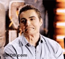A Man In A Blue Shirt Is Making A Funny Face While Sitting Down . GIF