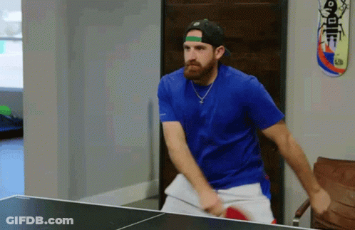 A Man In A Blue Shirt Is Playing Ping Pong With A Skateboard On The Wall GIF