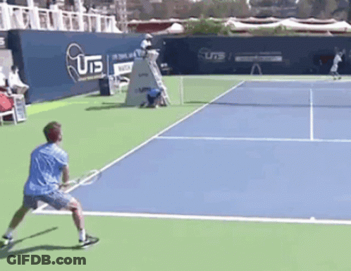 A Man In A Blue Shirt Is Playing Tennis On A Court With A U15 Sign In The Background GIF
