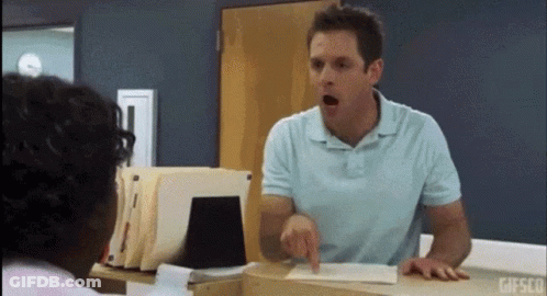 A Man In A Blue Shirt Is Pointing At Another Man In A Room . GIF