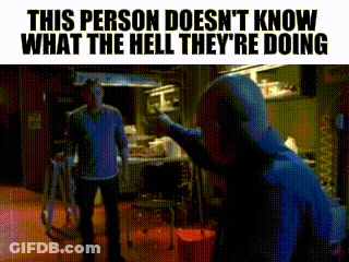 A Man In A Blue Shirt Is Pointing At Another Man In A Room . GIF