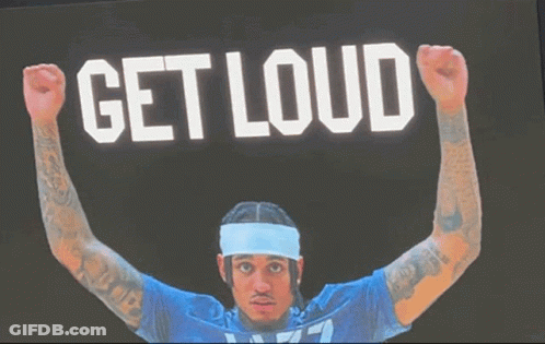 A Man In A Blue Shirt Is Raising His Fist In The Air In Front Of A Sign That Says " Get Loud " GIF