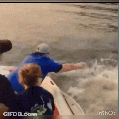A Man In A Blue Shirt Is Riding A Boat In The Ocean . GIF