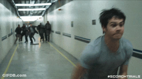 A Man In A Blue Shirt Is Running Down A Hallway With #Scorchtrials On The Bottom GIF