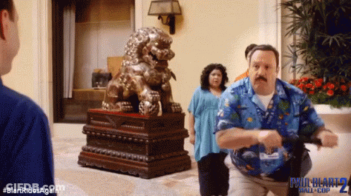 A Man In A Blue Shirt Is Running In Front Of A Statue Of A Lion .. GIF