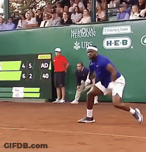 A Man In A Blue Shirt Is Running On A Tennis Court In Front Of A Memorial Hermann Banner GIF