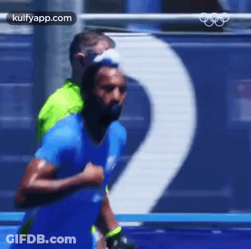 A Man In A Blue Shirt Is Running On A Track With A Man In A Green Shirt Behind Him . GIF