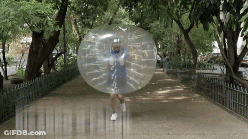 A Man In A Blue Shirt Is Running Through A Clear Bubble On A Sidewalk GIF