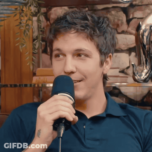 A Man In A Blue Shirt Is Singing Into A Microphone With A Tattoo On His Wrist GIF