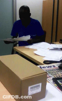A Man In A Blue Shirt Is Sitting At A Desk With A Box That Says News GIF