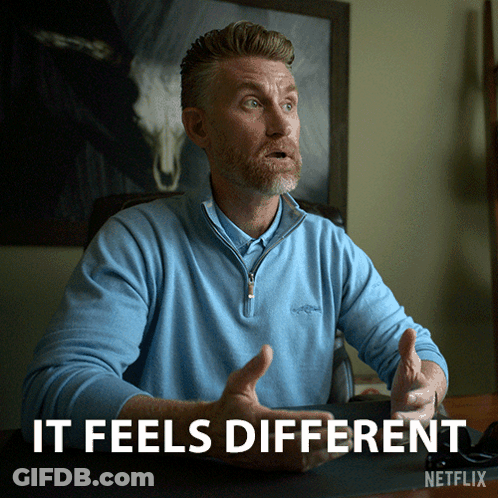 A Man In A Blue Shirt Is Sitting At A Desk With The Words " It Feels Different " Above Him GIF