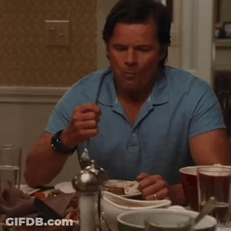 A Man In A Blue Shirt Is Sitting At A Table Eating Something GIF