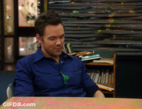 A Man In A Blue Shirt Is Sitting At A Table In Front Of A Stack Of Books GIF