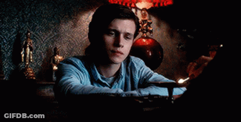A Man In A Blue Shirt Is Sitting At A Table With A Lamp . GIF