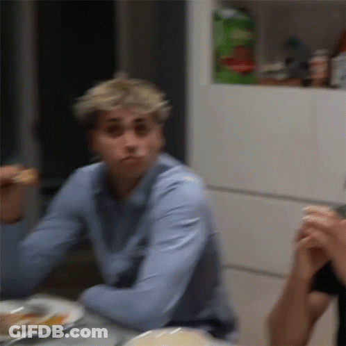 A Man In A Blue Shirt Is Sitting At A Table With A Plate Of Food . GIF