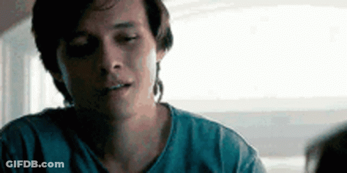 A Man In A Blue Shirt Is Sitting At A Table With His Eyes Closed And Looking At Something . GIF