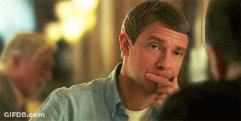 A Man In A Blue Shirt Is Sitting At A Table With His Hand To His Chin . GIF