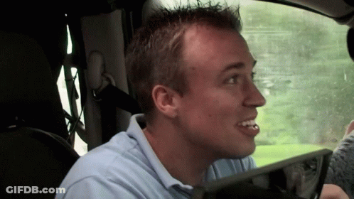 A Man In A Blue Shirt Is Sitting In A Car With His Mouth Open GIF