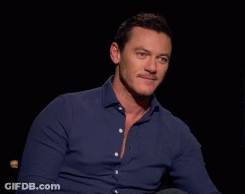 A Man In A Blue Shirt Is Sitting In A Chair In A Dark Room GIF