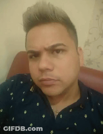 A Man In A Blue Shirt Is Sitting In A Chair Making A Funny Face GIF