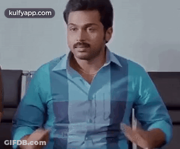 A Man In A Blue Shirt Is Sitting In A Chair Talking To Someone . GIF