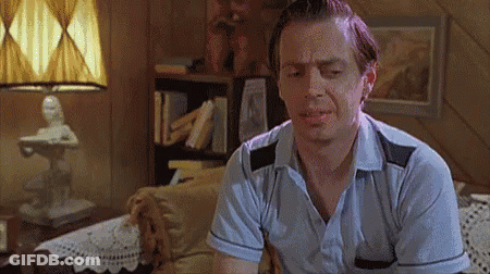 A Man In A Blue Shirt Is Sitting In A Living Room With A Lamp . GIF