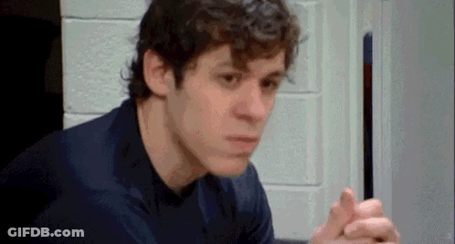 A Man In A Blue Shirt Is Sitting In A Room With His Hands Folded . GIF