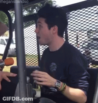 A Man In A Blue Shirt Is Sitting In A Vehicle Behind A Fence . GIF