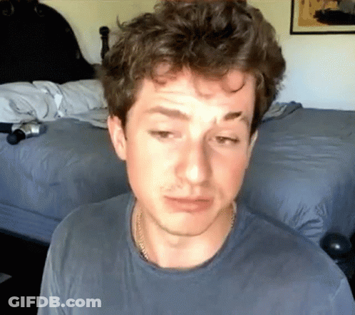 A Man In A Blue Shirt Is Sitting In Front Of A Bed With His Eyes Closed GIF